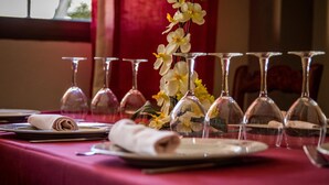 Una mesa dispuesta con copas de vino, platos y un mantel enrollado, con un jarrón de flores en el centro.