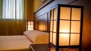 Una habitación de hotel con una cama, una mesita de noche y una linterna tradicional al estilo japonés que proporciona luz cálida.
