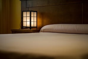 A neatly made bed with a wooden nightstand beside it, featuring a traditional-style wall-mounted lamp. - El Nacimiento (Deifontes)