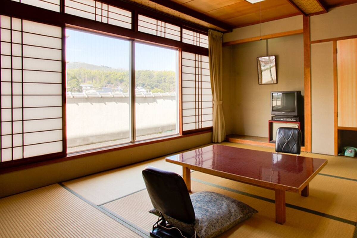 A traditional Japanese room with tatami flooring, a low table, a cushion, a television, and sliding doors.