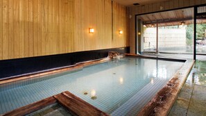 A traditional Japanese onsen with a wooden interior, a tiled pool, and a view of the outdoors. - Ryotei Yamanoi Hotel (Matsue)