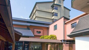 Un edifici tradicional japonès amb un teulat inclinat, una finestra en forma de cor i una petita zona de jardí.