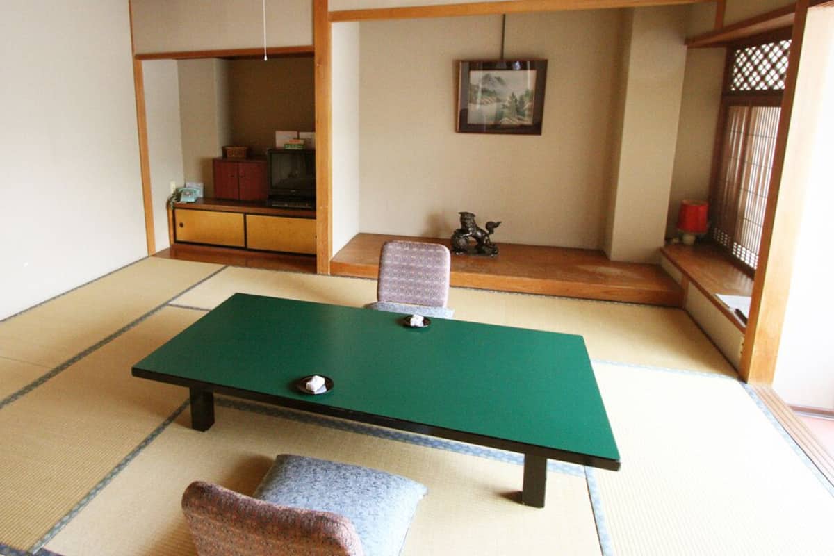 A tatami mat room with a green futon, a small table with a tea set, a cabinet with a television, and a decorative horse statue.
