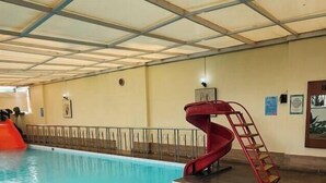 An indoor swimming pool with a red slide and a ladder. - Alia Cikini (Jakarta)