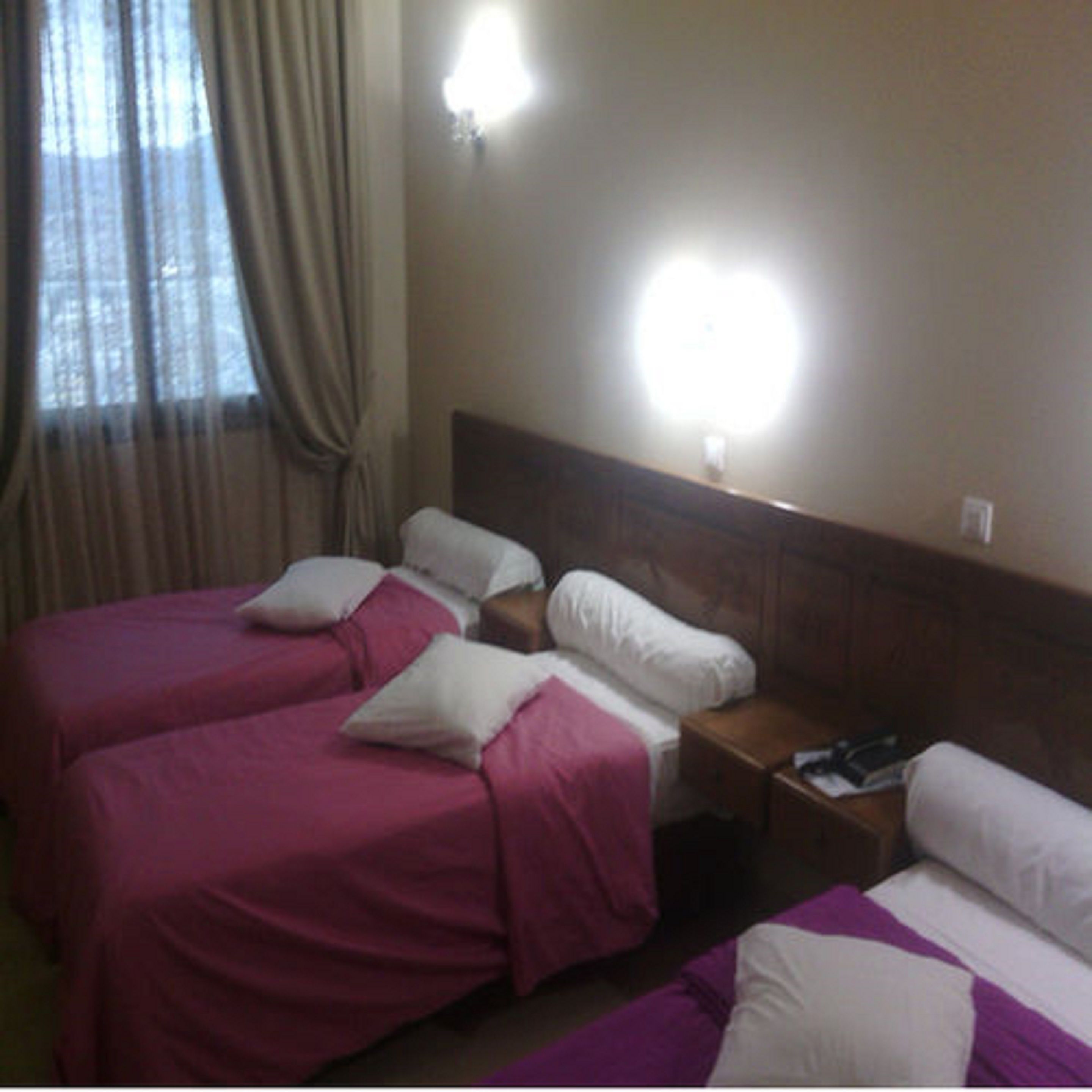 A hotel room with two beds, each with a wooden headboard, and a nightstand between them.