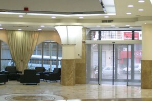 A lobby with a reception desk, seating area, and a glass door entrance. - Le Cristal Hotel (Béjaïa)
