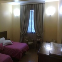 Una habitación de hotel con dos camas, una mesita, una silla y una ventana con cortinas.