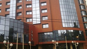 Ett hotell med flera våningar, en modern fasad av glas, en väl synlig entré och en parkeringsplats med bilar.