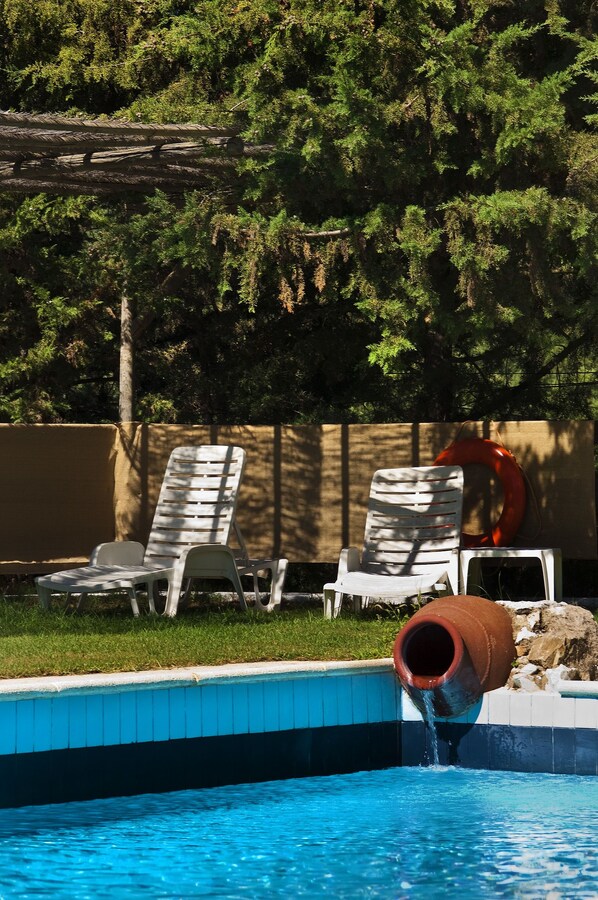 Une piscine dotée d’une fontaine, de deux chaises longues blanches et d’un toboggan rouge.