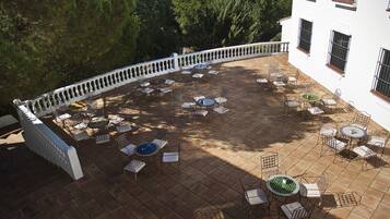 Un patio al aire libre con varias mesas y sillas redondas, rodeado por una barandilla blanca.