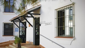 Un edificio blanco con puerta negra y rejas en las ventanas, un cartel que dice "El Encinar" y una escalera que lleva a la entrada.