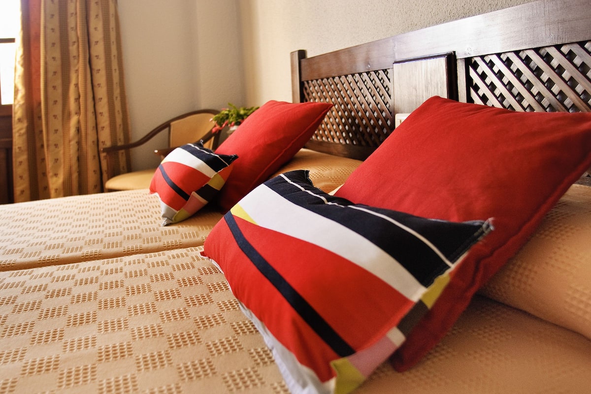 Un lit avec une couvre-lit à motifs et plusieurs oreillers, dont un rouge et un à rayures.