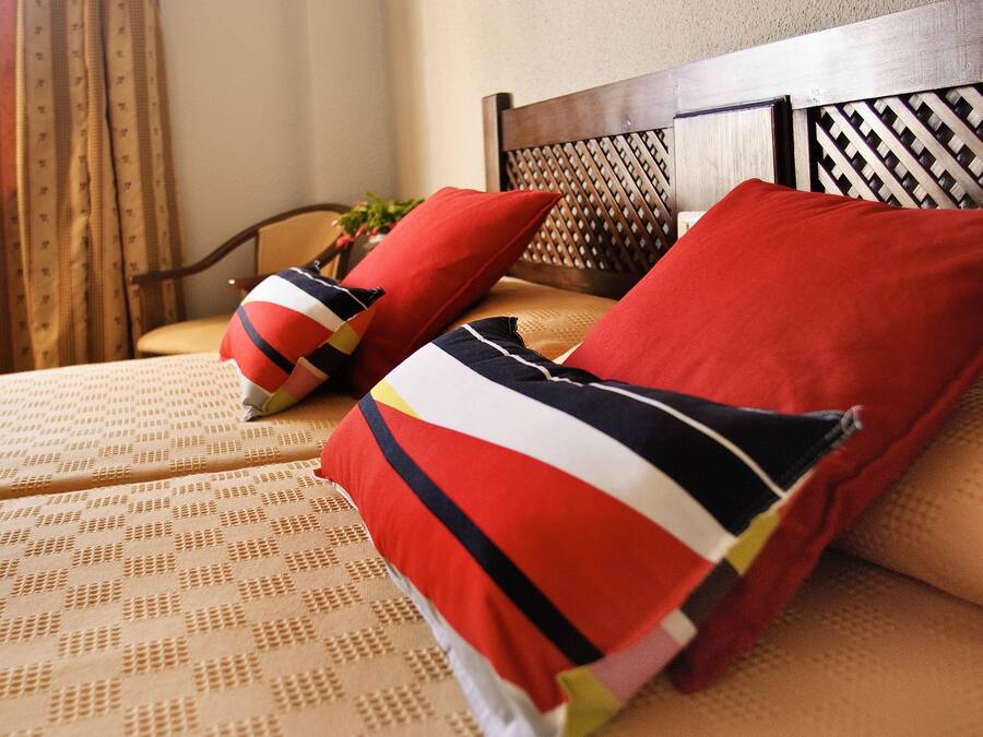 A bed with a patterned bedspread and multiple pillows, including a red one and a striped one.