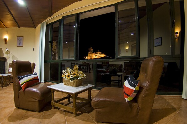 Una habitación con dos sillones de cuero, una mesita y un ventanal con vistas a un edificio iluminado en la noche.