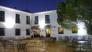 Un patio con mesas al aire libre y un edificio blanco con varias ventanas y puertas.