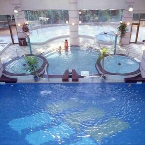 Una piscina interior con dos jacuzzis, una zona de natación central y vistas al exterior.