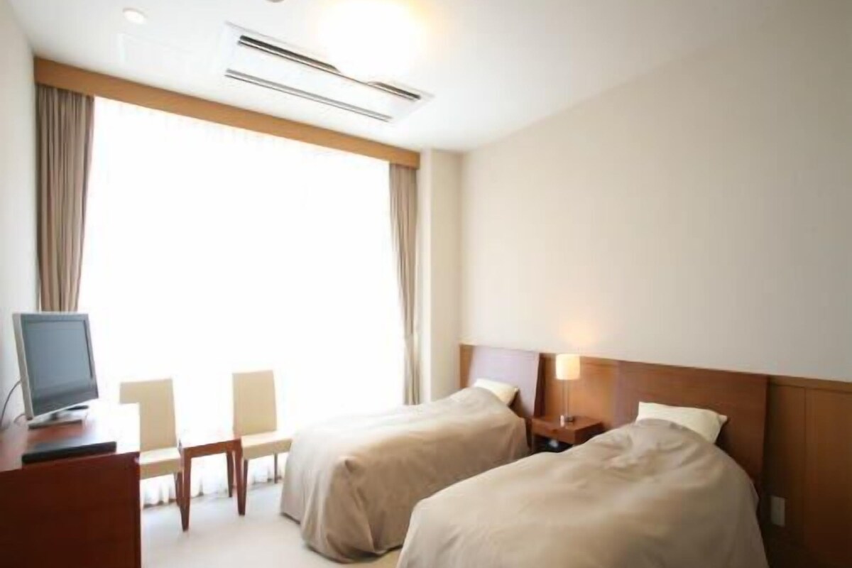 Habitación de hotel con dos camas, un escritorio con computadora, una silla y una ventana con cortinas.