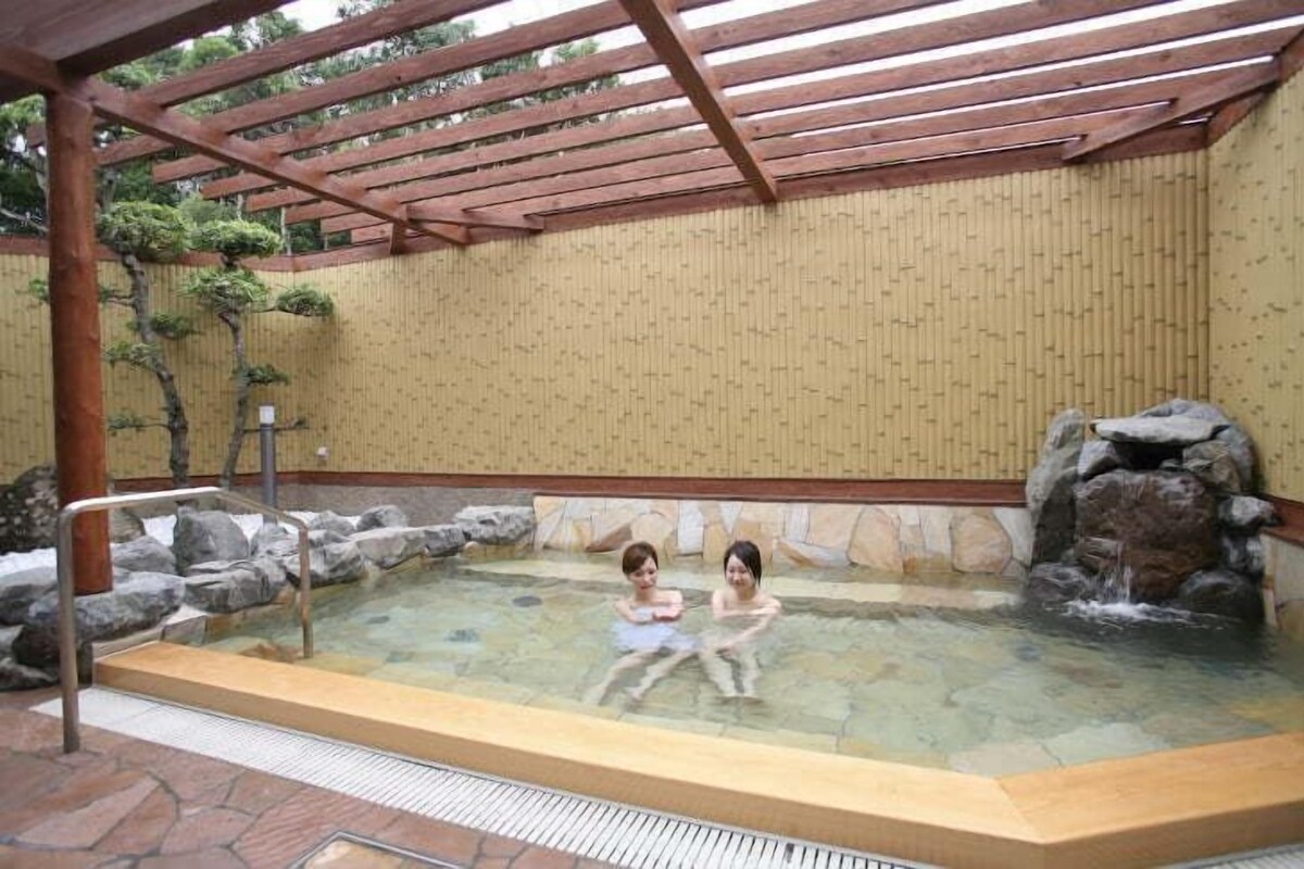Un área de aguas termales con una pérgola de madera, escalones de piedra y una pequeña cascada.