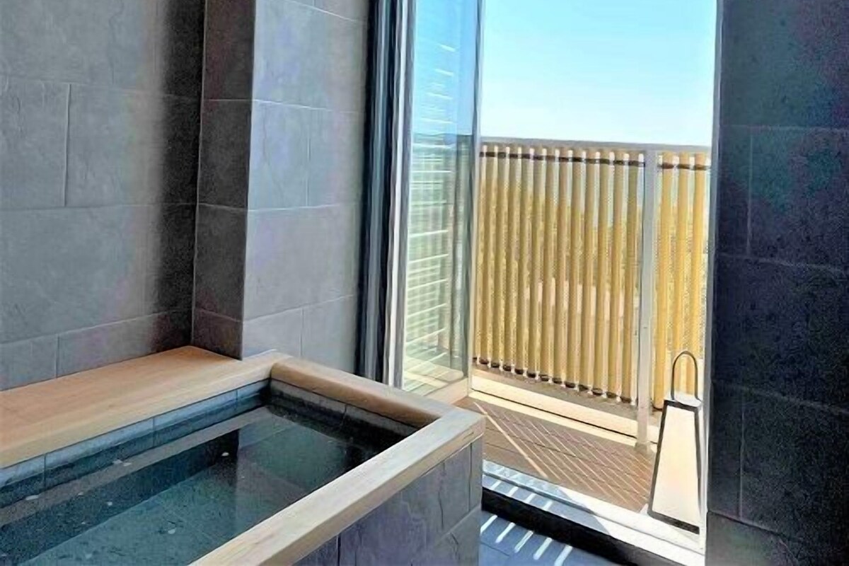 Un baño moderno con ducha envuelta en vidrio, un banco de madera y vistas a un balcón con barandilla.