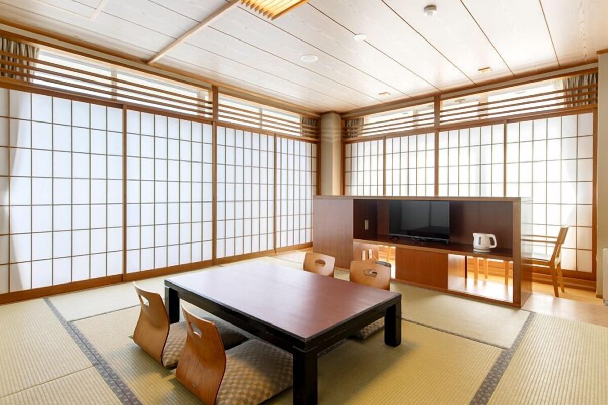 Una habitación japonesa tradicional con suelo de tatami, una mesa baja, asientos y un televisor.
