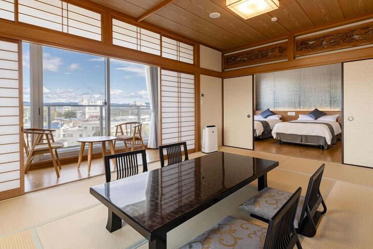 Una habitación tradicional japonesa con suelo de tatami, una mesa baja y vistas a la ciudad.