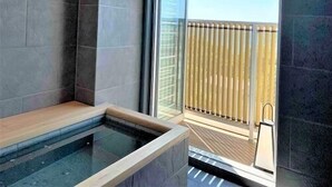 A modern bathroom with a glass-enclosed shower, a wooden bench, and a view of a balcony with a railing. - Kurhouse Shirahama (Shirahama)