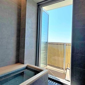 Un baño moderno con ducha envuelta en vidrio, un banco de madera y vistas a un balcón con barandilla.