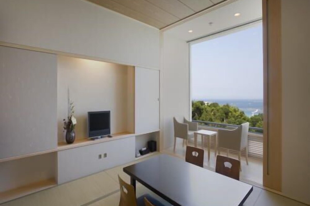 Un interior moderno con una mesa de comedor, sillas, un televisor en un estante y un balcón con vistas.
