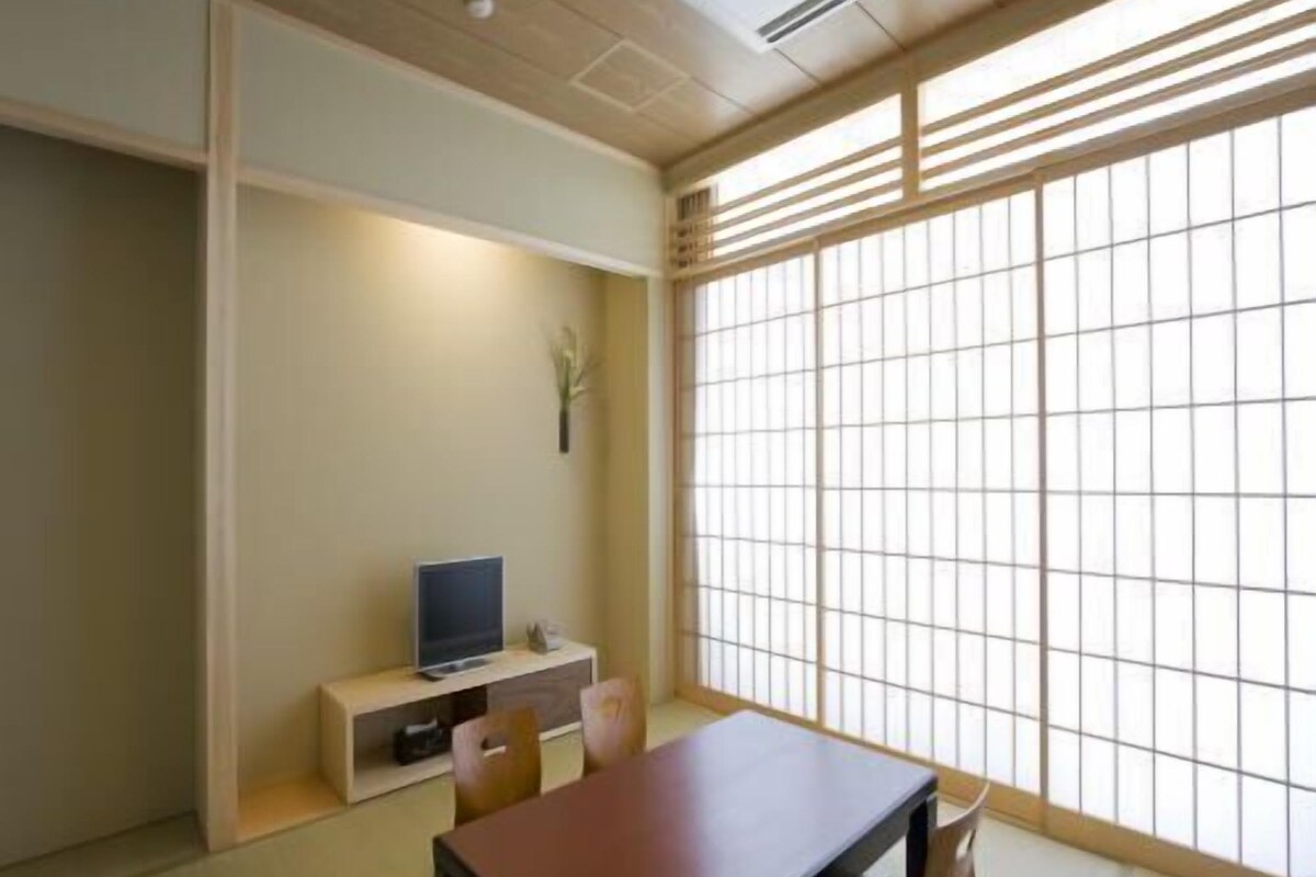 Una habitación japonesa tradicional con suelo de tatami, una mesa baja, un televisor sobre un pedestal y un gran shoji.