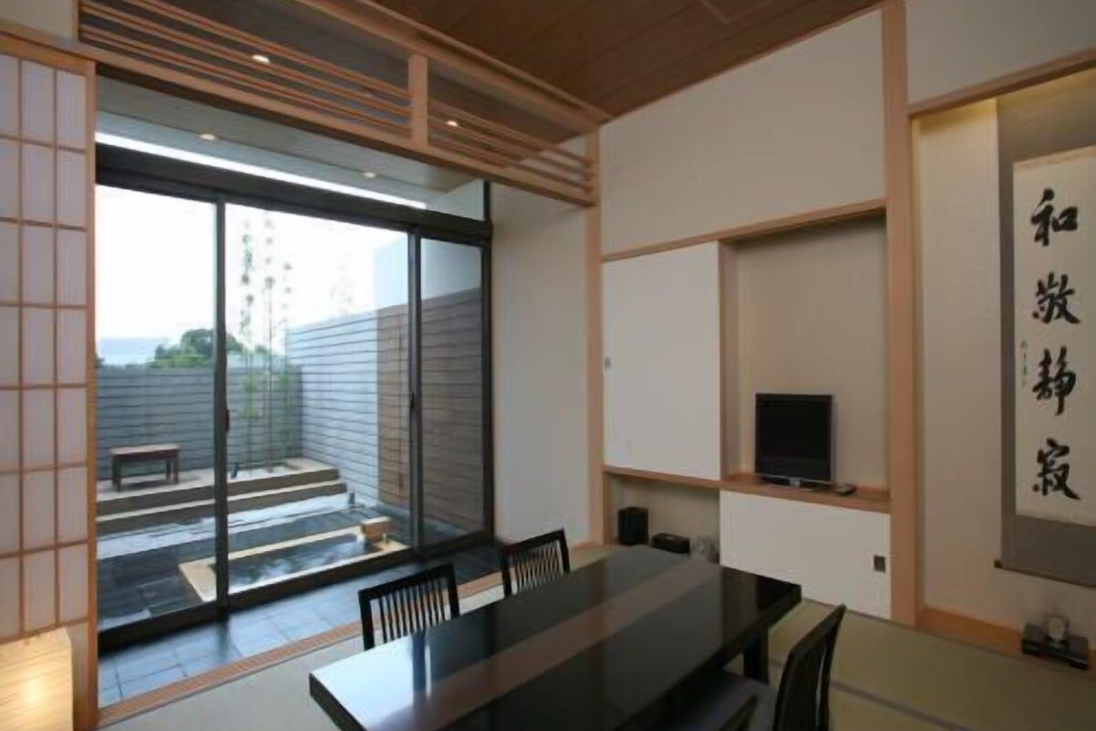 Un interior moderno con una mesa de comedor, sillas, un televisor y una puerta corrediza de vidrio que da a un espacio exterior.