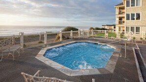 Una piscina con vista al océano, rodeada de sillones de descanso y un edificio con varios balcones.