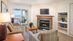 Una sala de estar con chimenea, sofá, sillón y televisor colocado sobre la chimenea.