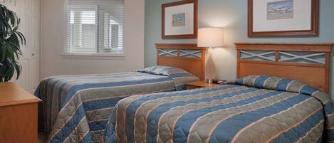 A room with two beds, a nightstand, a lamp, and framed pictures on the wall.