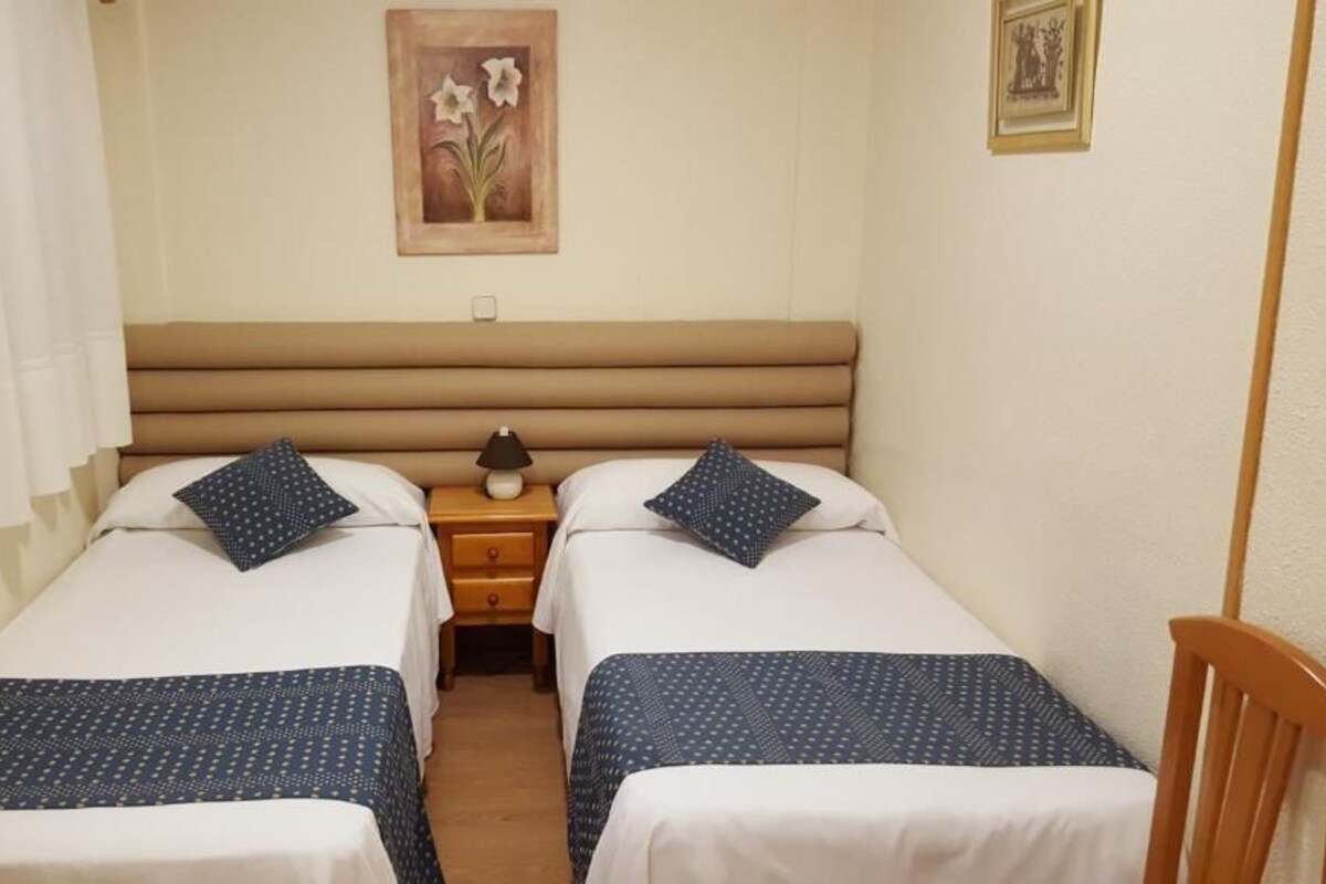 A double room with two beds, each with a pillow and a lamp on a bedside table.
