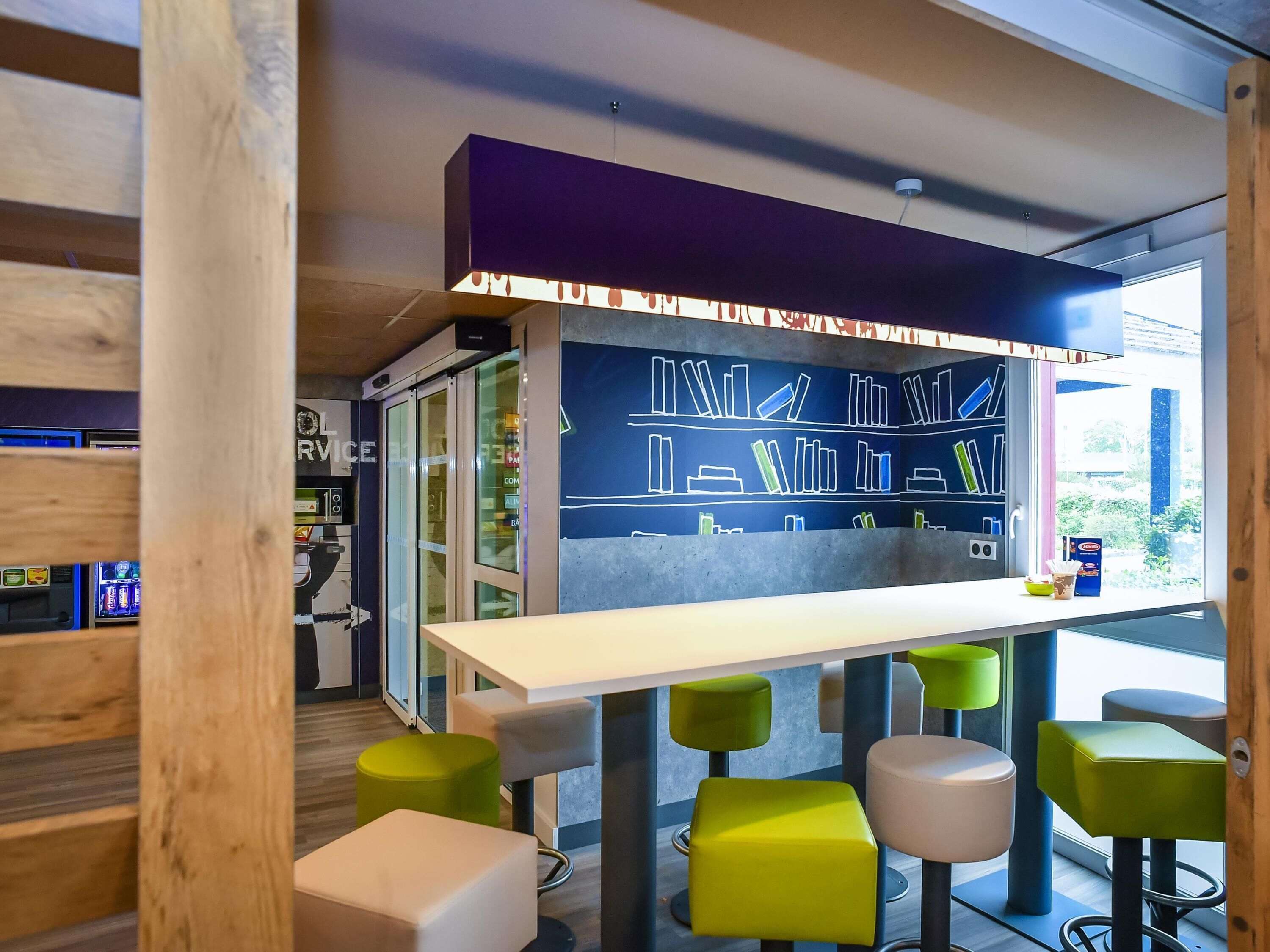 A modern bar area with a chalkboard menu, green bar stools, and a view of the outdoors.