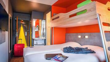 A hotel room with a bunk bed, a single bed, a suitcase, and a magazine on the bed.