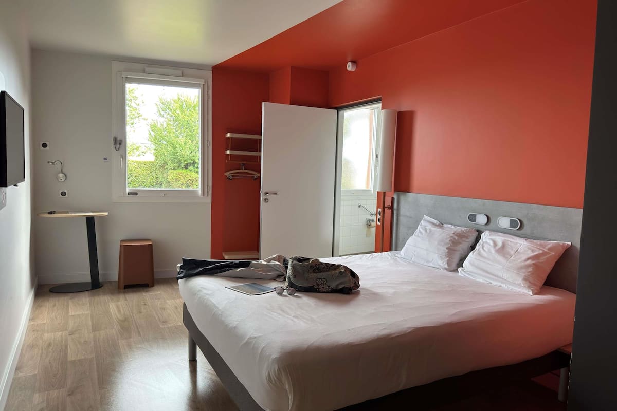 A bedroom with a bed, a wardrobe, a small table, and a window.