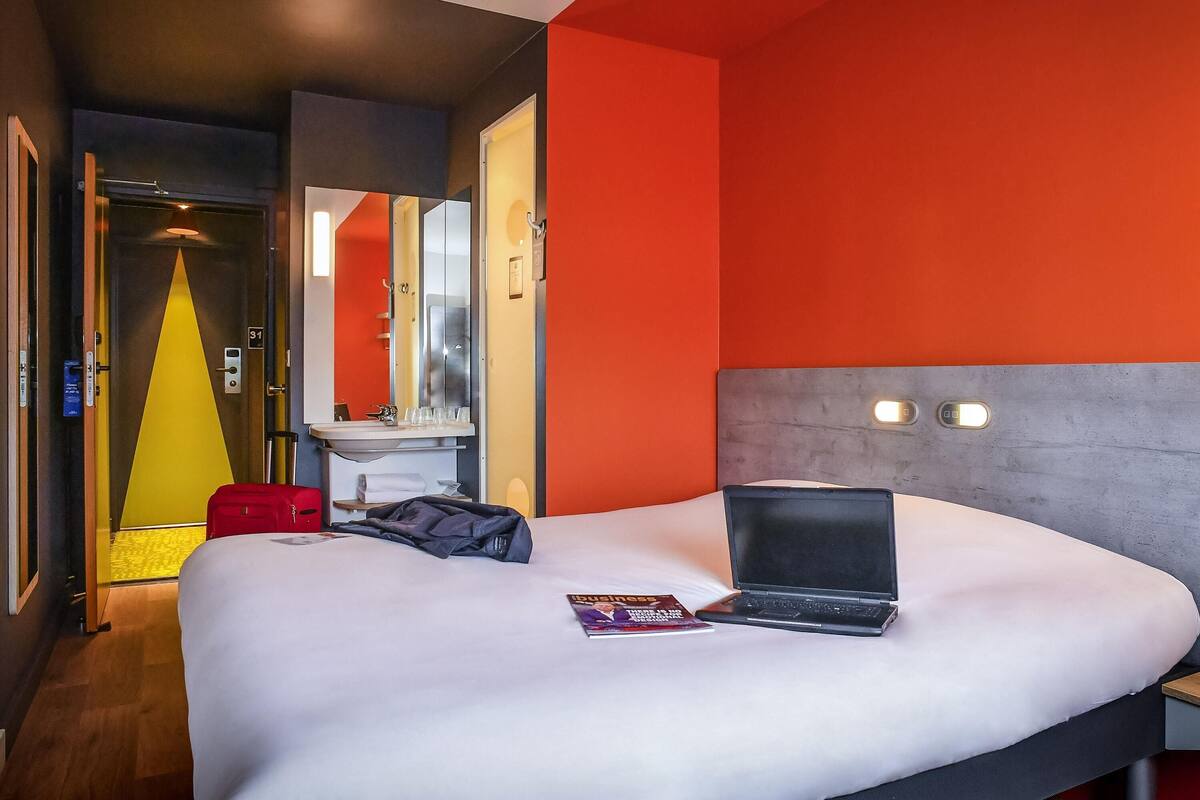 A hotel room with a bed, a laptop, and a magazine on the bed.