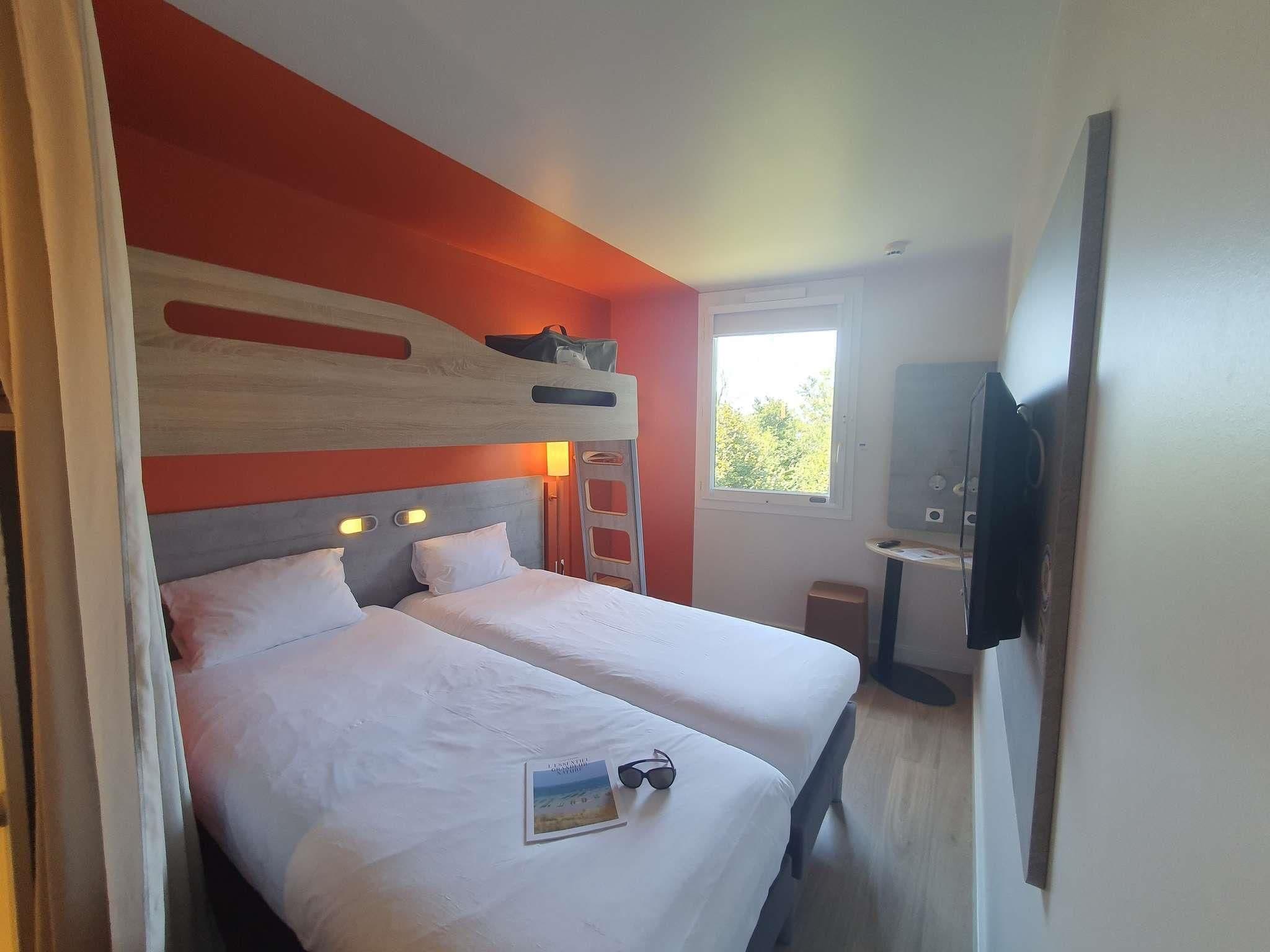 Une chambre avec deux lits, une fenêtre, un téléviseur et une échelle.
