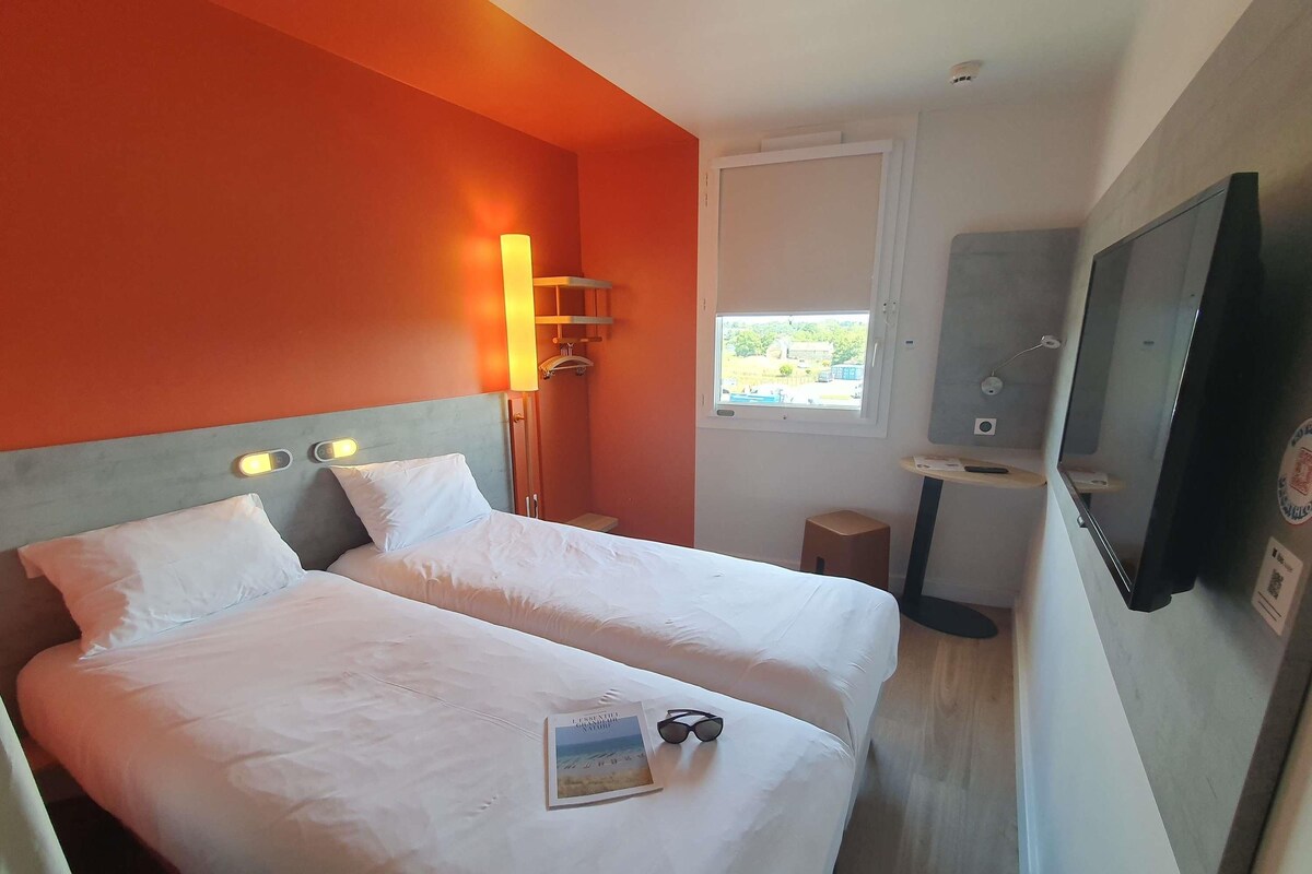 A hotel room with two beds, a TV, a window, and a small table.