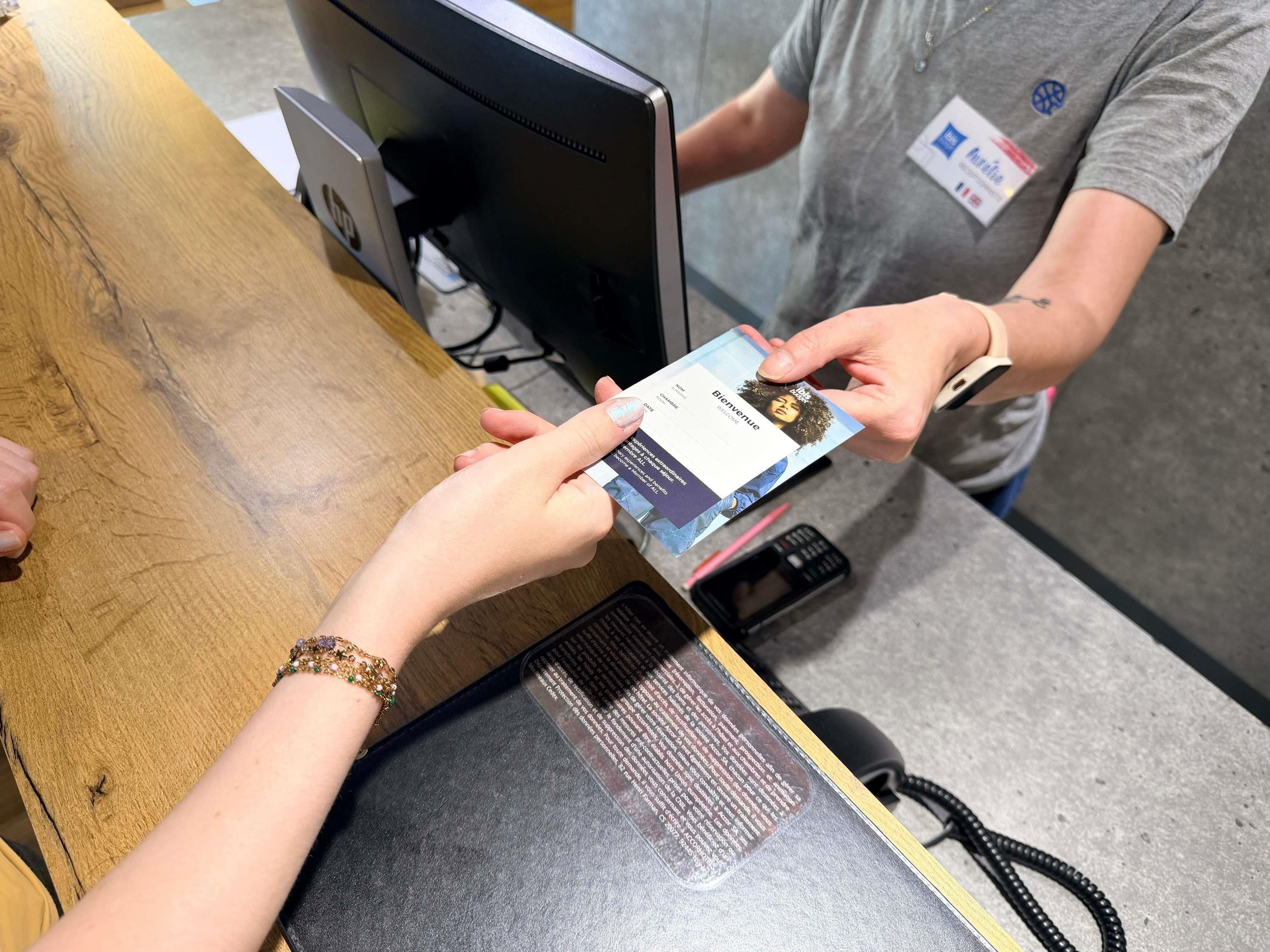 A person holding a card at a counter with a computer monitor and a telephone.