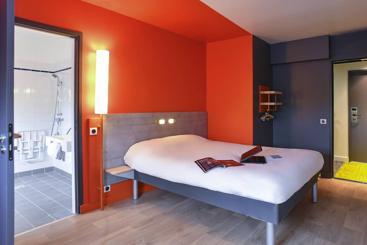 A modern hotel room with a bed, bedside table, and a bathroom with a shower.
