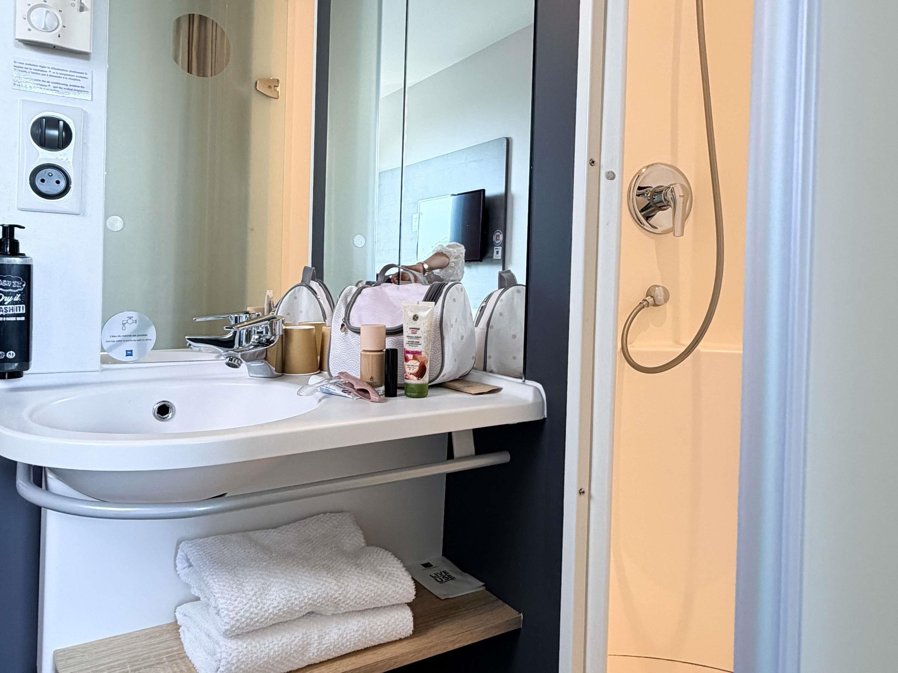 A bathroom with a white sink, a mirror, a towel rack, and a shower area.