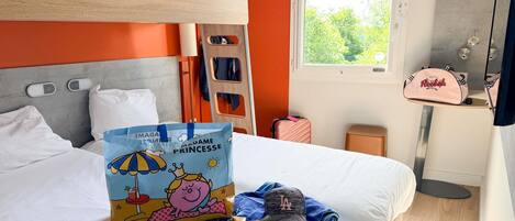 Habitación de hotel con literas, una ventana que da a árboles, una mesita de noche con una bolsa Reebok y una bolsa con un personaje de dibujos animados.