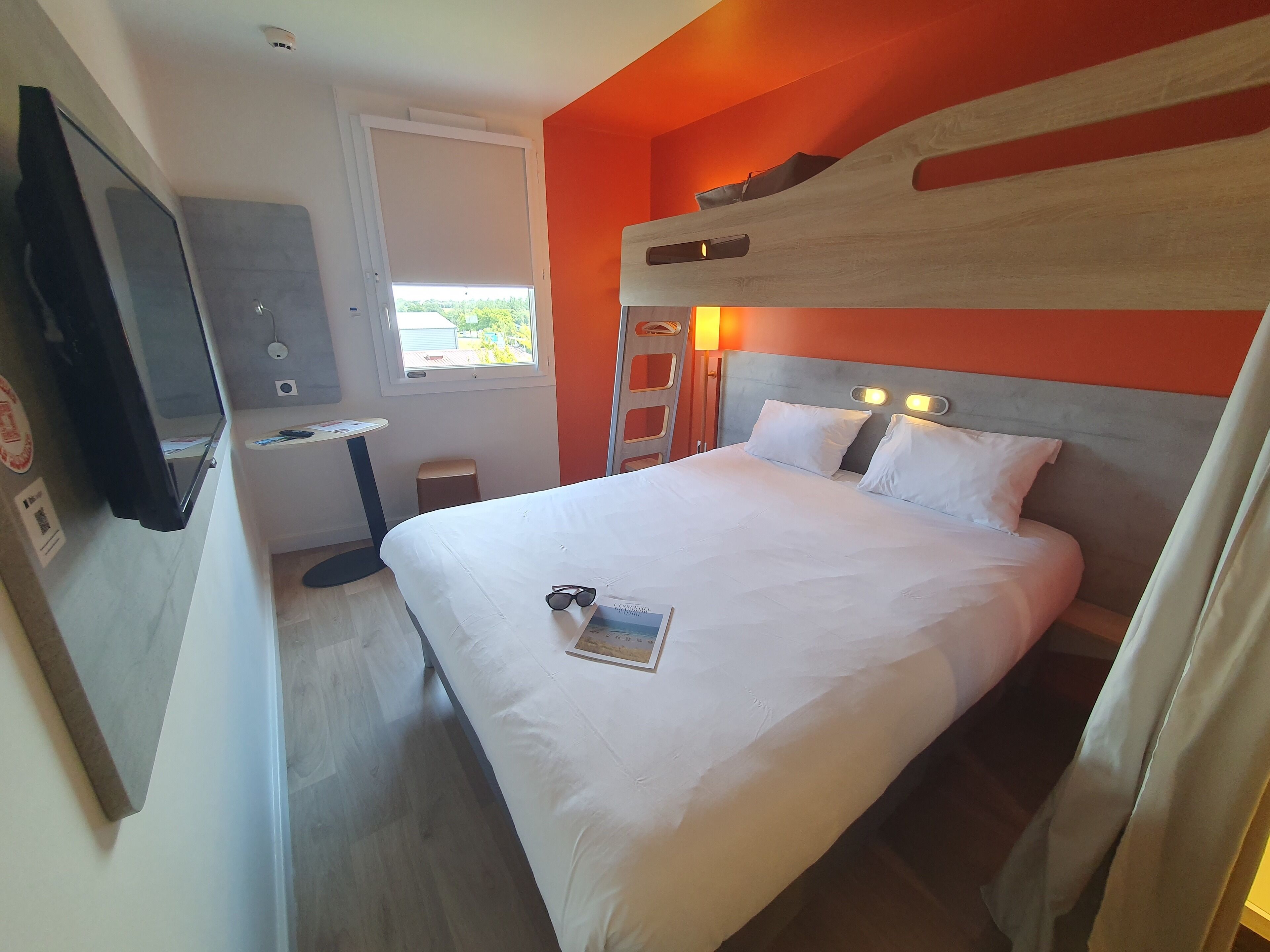 A hotel room with a bed, a desk, a chair, a TV, and a window.