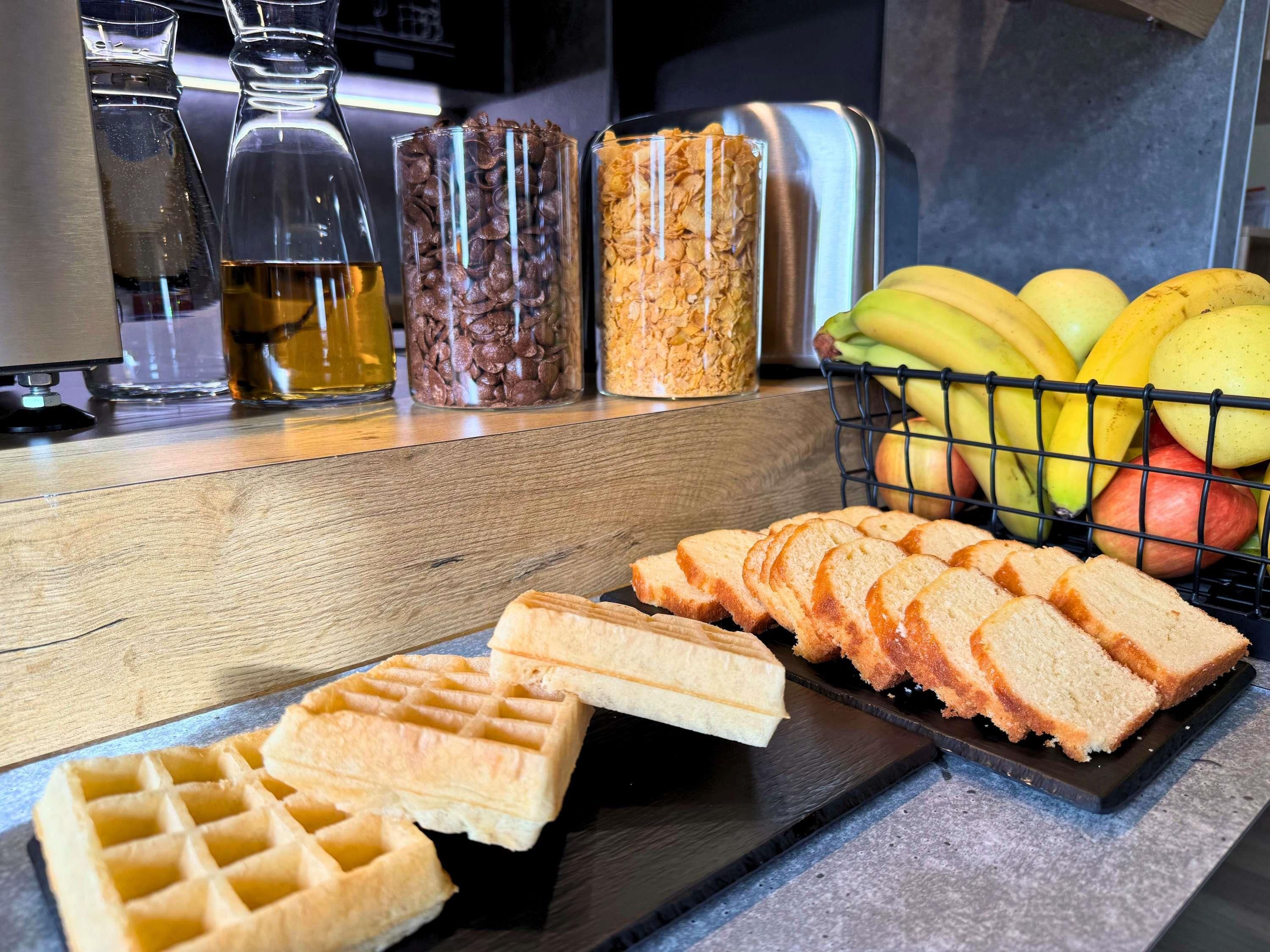 A kitchen counter with waffles, sliced bread, and a fruit basket.