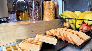 A kitchen counter with waffles, sliced bread, and a fruit basket.