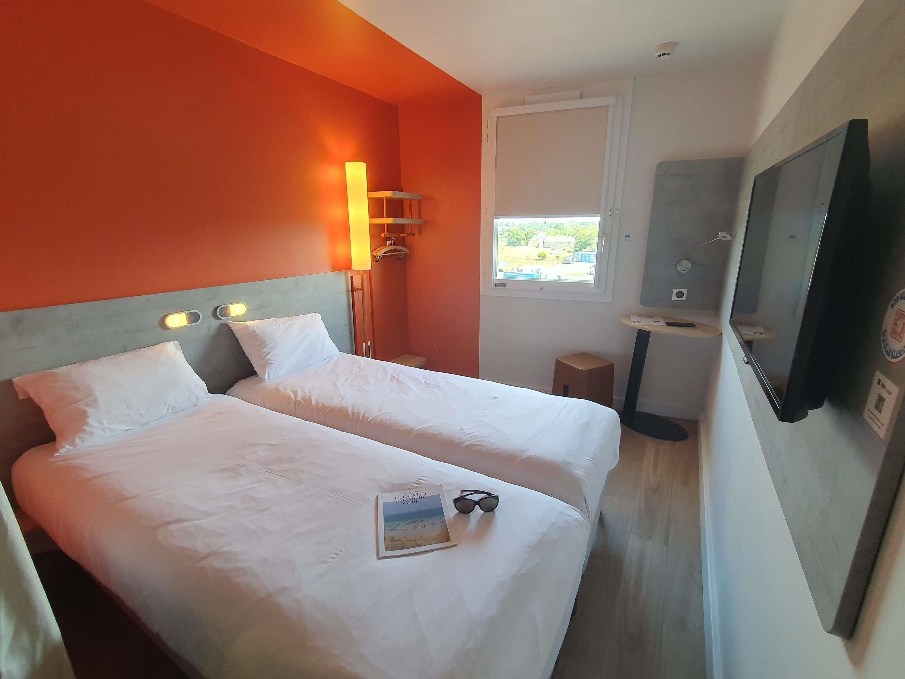 Hotellihuone, jossa on kaksi sänkyä, televisio, ikkuna ja pieni pöytä.