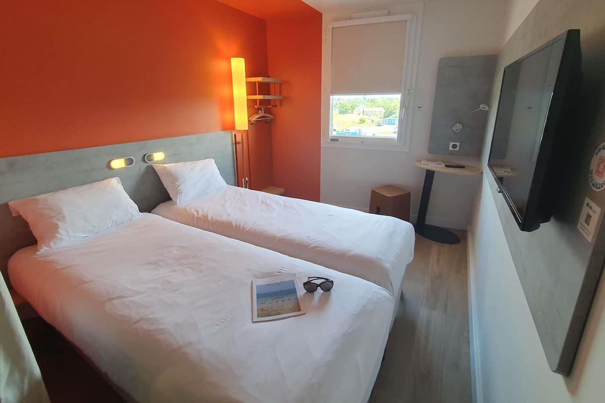 Hotellihuone, jossa on kaksi sänkyä, televisio, ikkuna ja pieni pöytä.