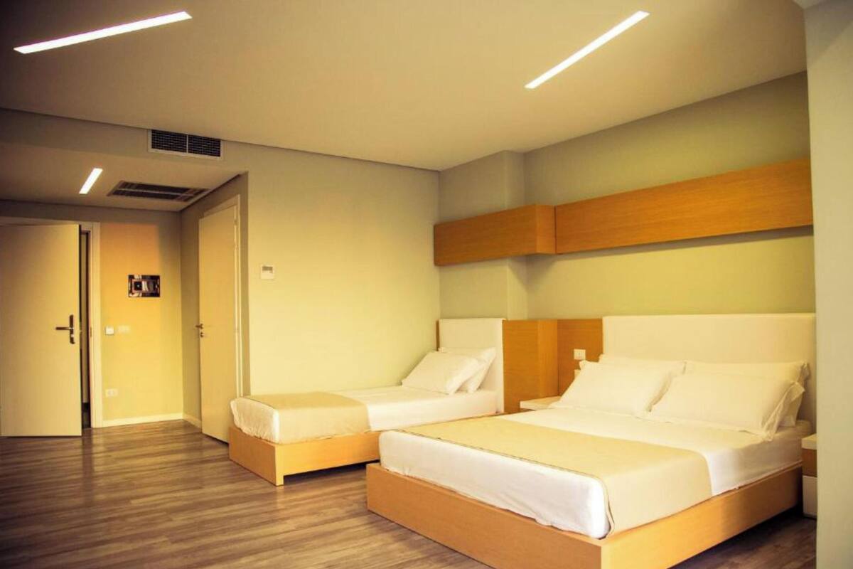 A hotel room with two beds, wooden headboards, a door, and a light switch on the wall.